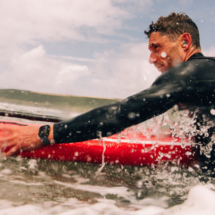 Surfer in water on a red surf board wearing an Apple watch