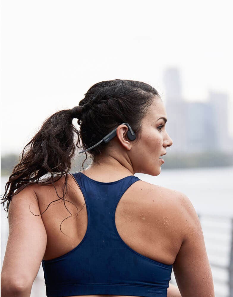 Shokz open-ear headphones worn by a jogging athlete