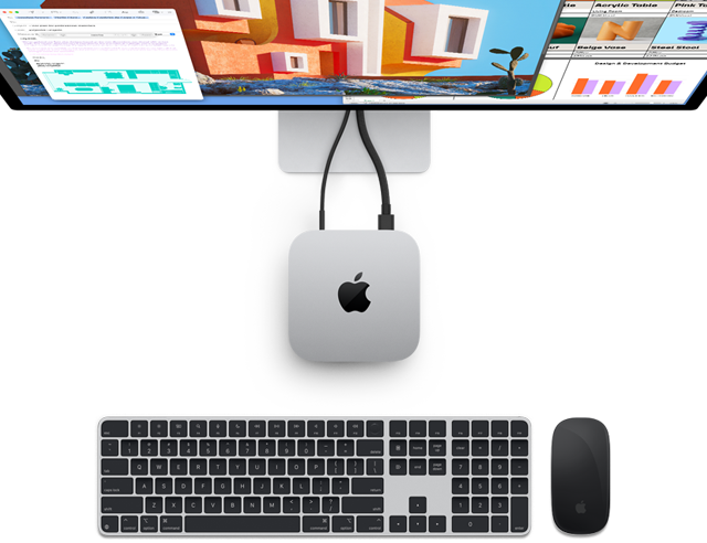 Top of silver Mac mini with Apple logo, shown plugged into a monitor and next to a wireless Magic Keyboard and Magic Mouse